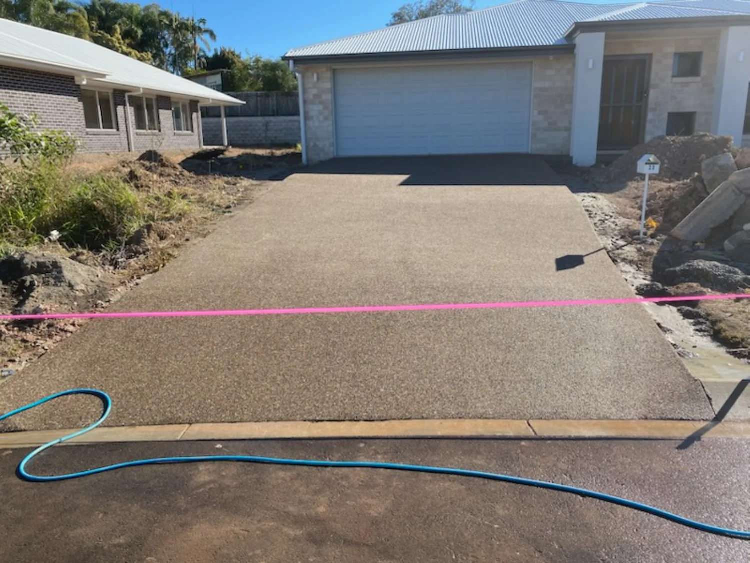 Exposed aggregate concrete driveway with pink ribbon visible by Mark Holstein Concreting