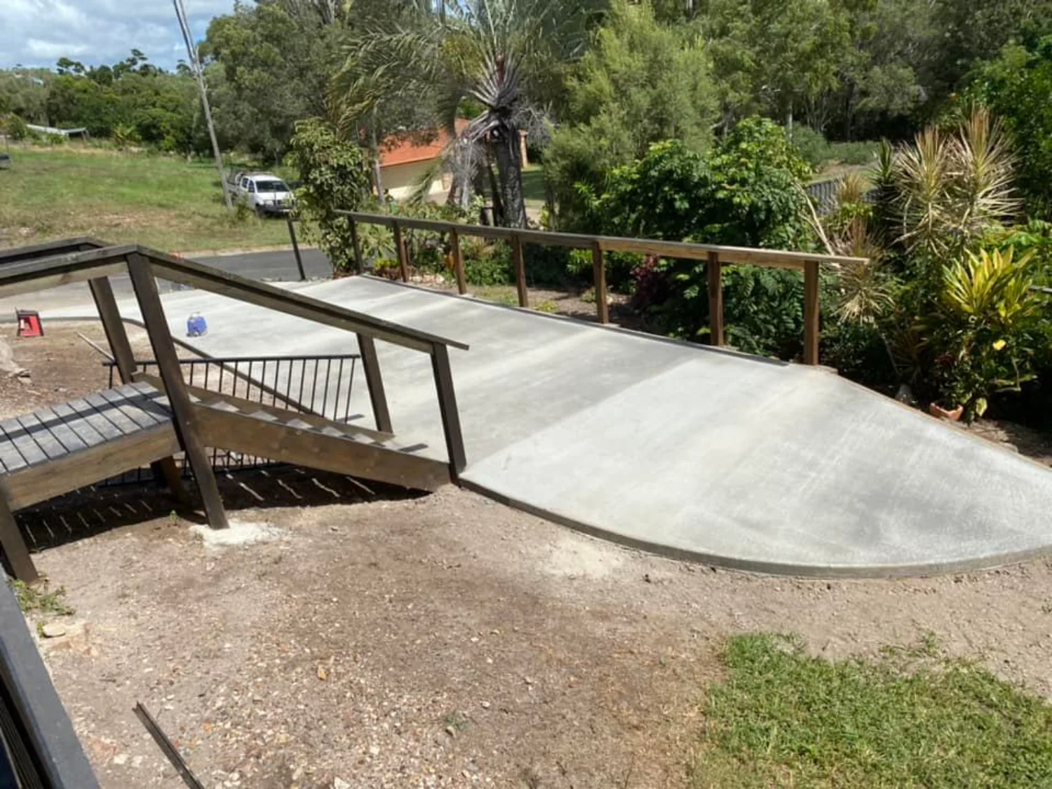 Concrete driveway installation next to a wooden staircase, created by Mark Holstein Concreting in Hervey Bay