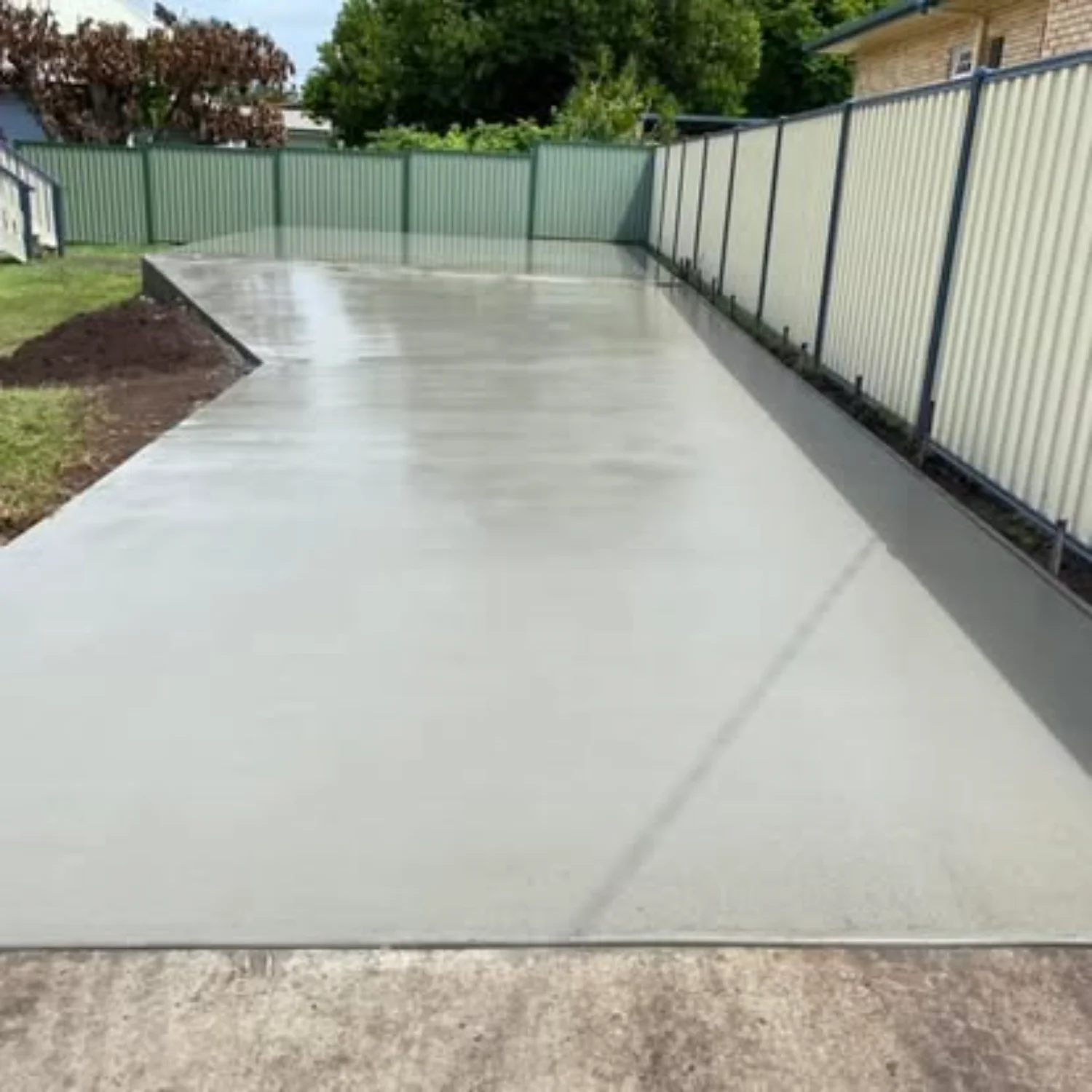 Concrete shed slab freshly poured and levelled next to a corrugated fence by Mark Holstein Concreting