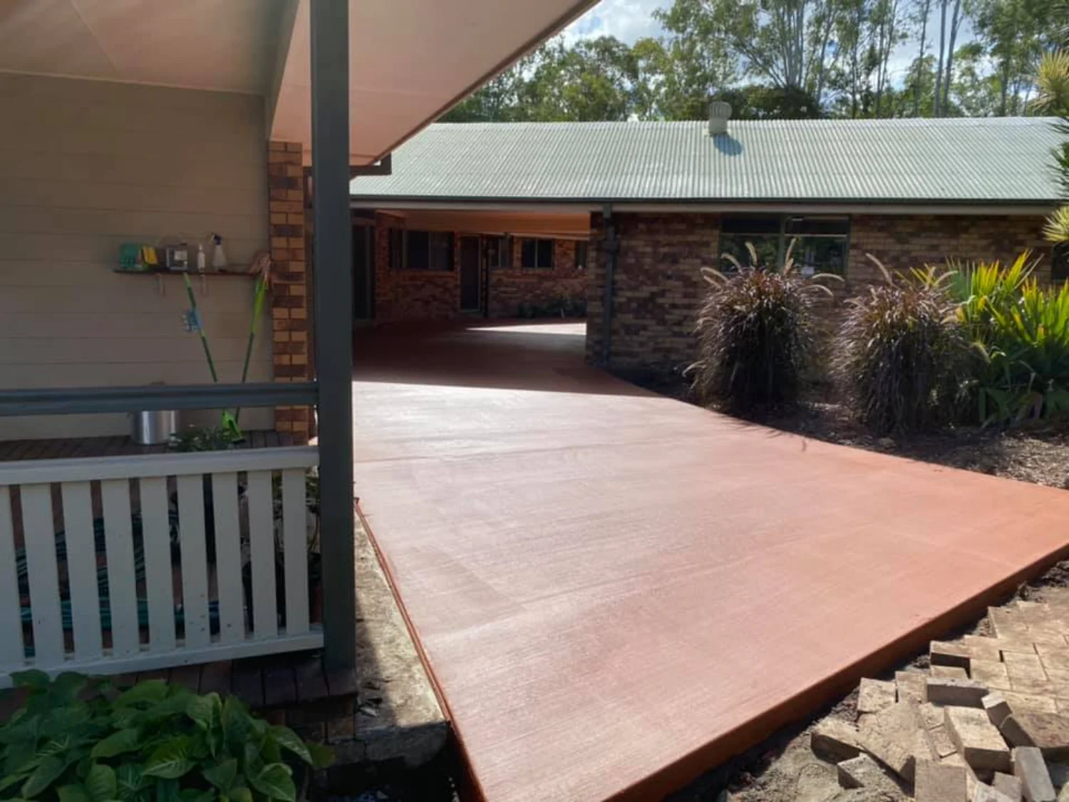 Ochre-coloured concrete extension connecting a brick building's rooms and deck by Mark Holstein Concreting in Hervey Bay
